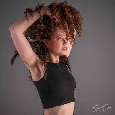 A white woman (Lucia) holds her curly carmel colored hair above her head so it cascades down over her face
