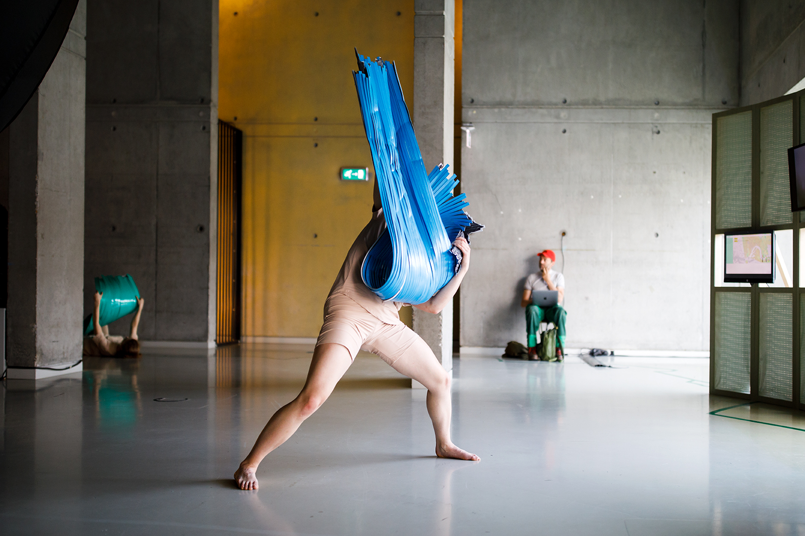 Dancer in nude costume holds a three dimensional blue object, obstructing their face.