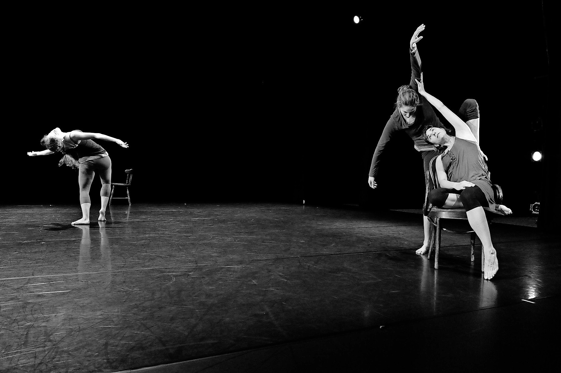 3 dancers moving on a stage, 2 are close together, 1 far away. Black and white image. 